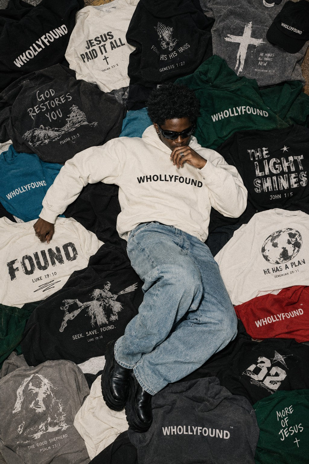 WHOLLYFOUND hoodie and tees laid out around a model in the studio